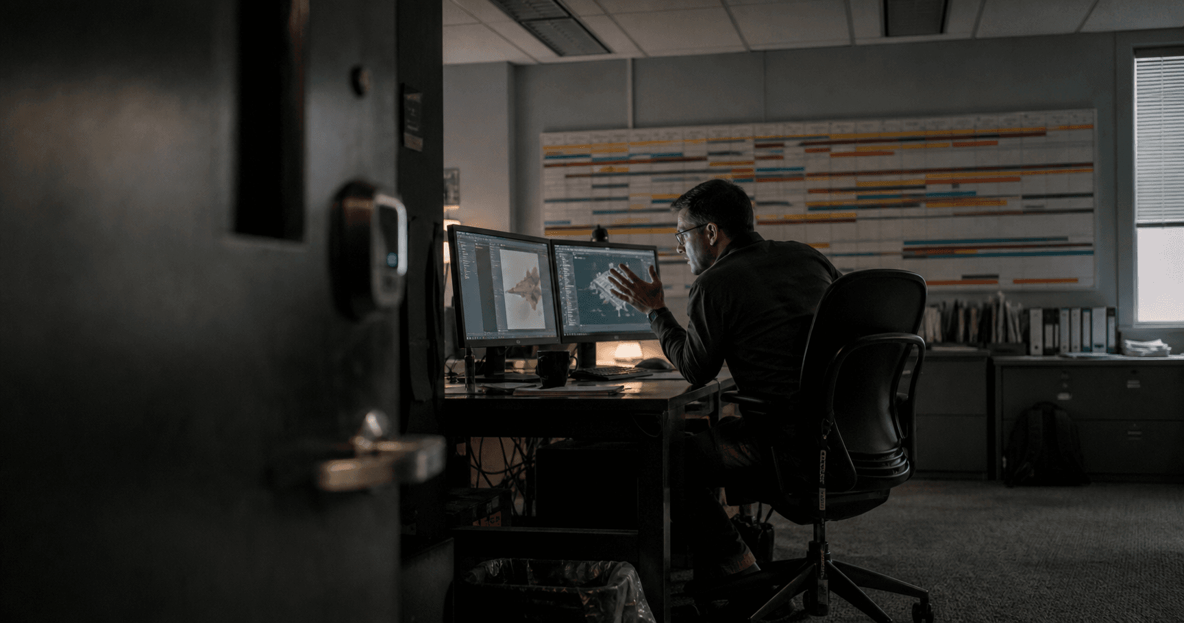 Tense engineer at glowing dual monitors, framed by dark open office door